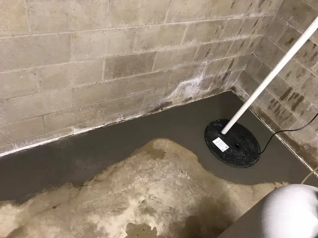 Floodwater in a basement around a mop and wringer bucket near a concrete wall.