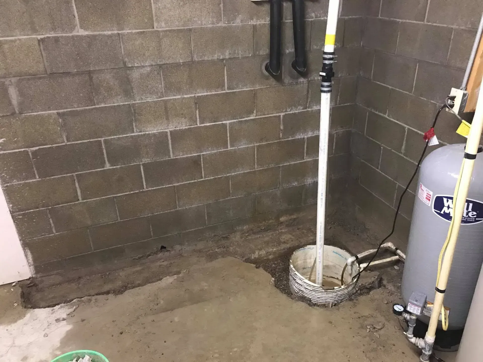 Basement utility corner with pipes, a bucket, and a water heater against cinder block walls.