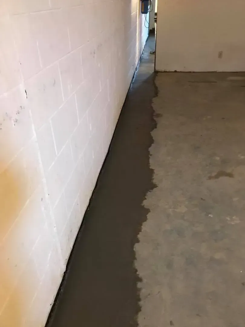 Narrow hallway with a white tiled wall and a wet, dark floor edge along the baseboard