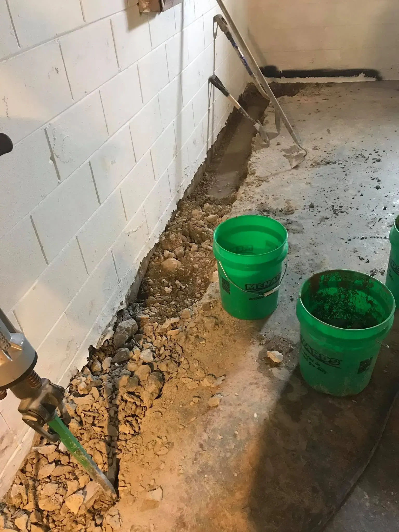 Dirty utility room floor with two green buckets and a mop near a tiled wall.