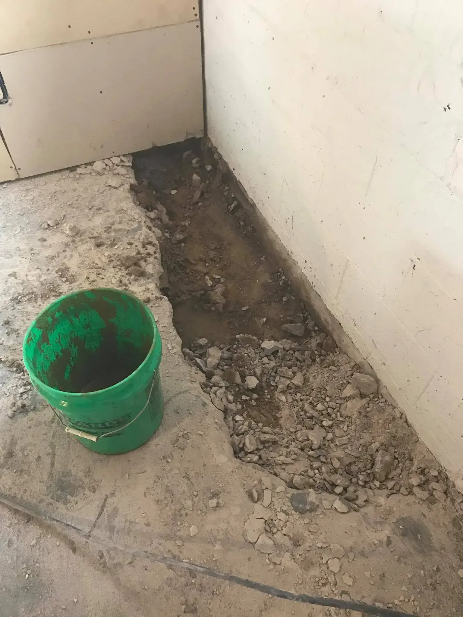 Green bucket beside a rough trench in a corner of a tiled room