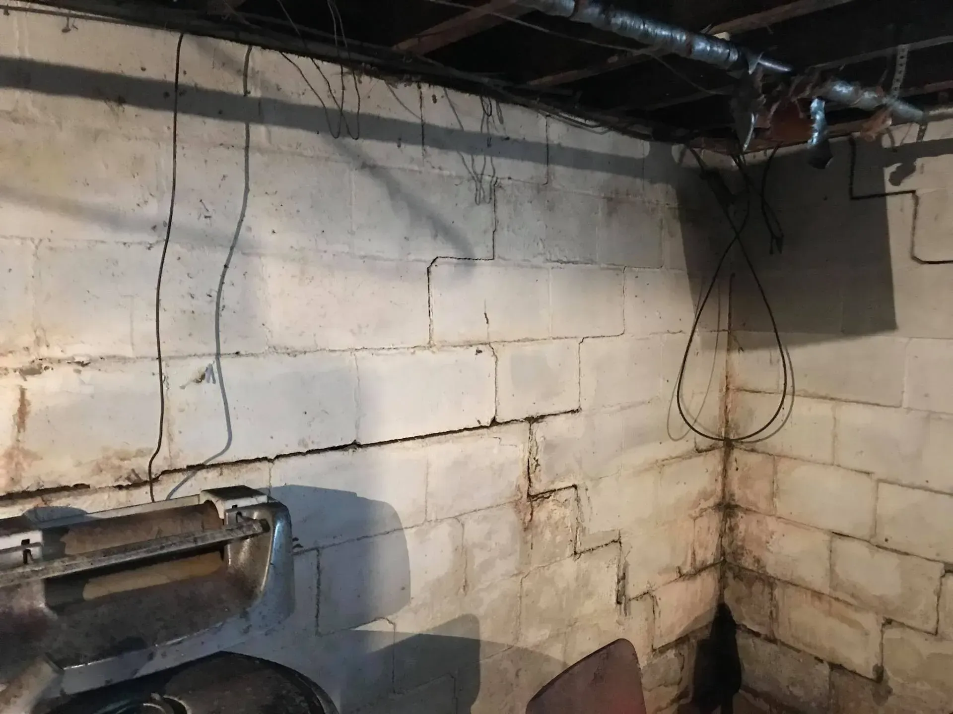 Dim basement with white cinder block walls, exposed pipes, and a dark corner with stains and wires