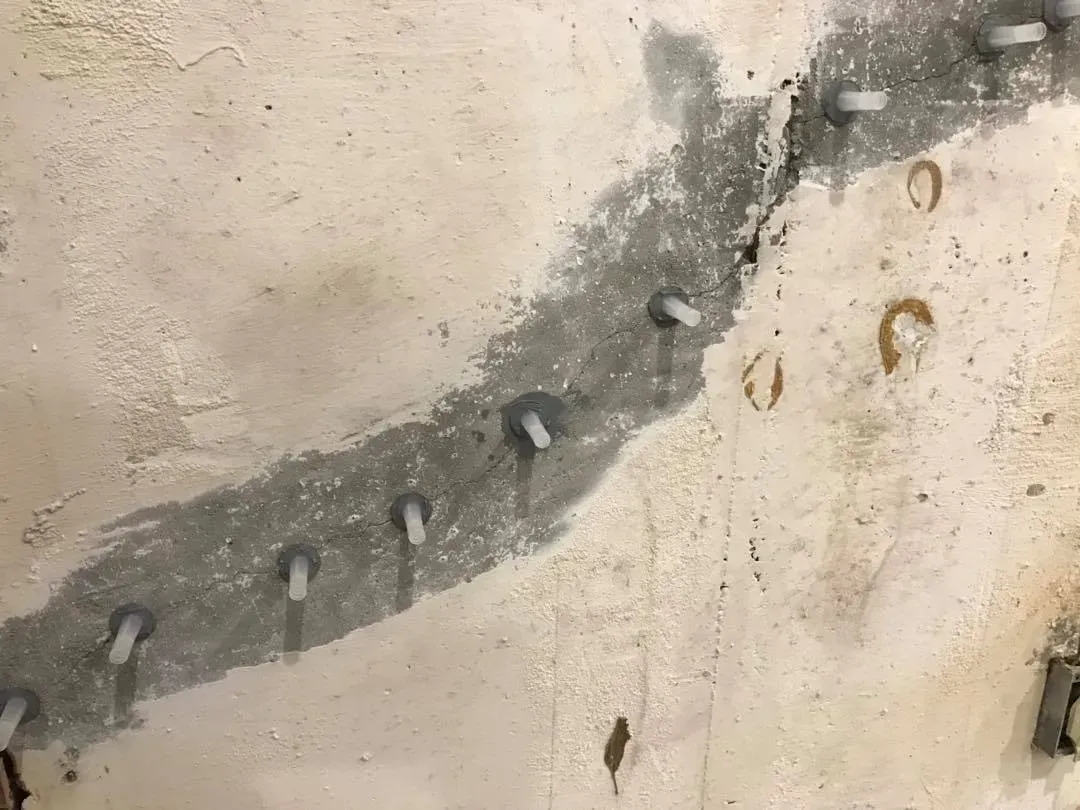 Small concrete repair patch with exposed bolts on a weathered wall section