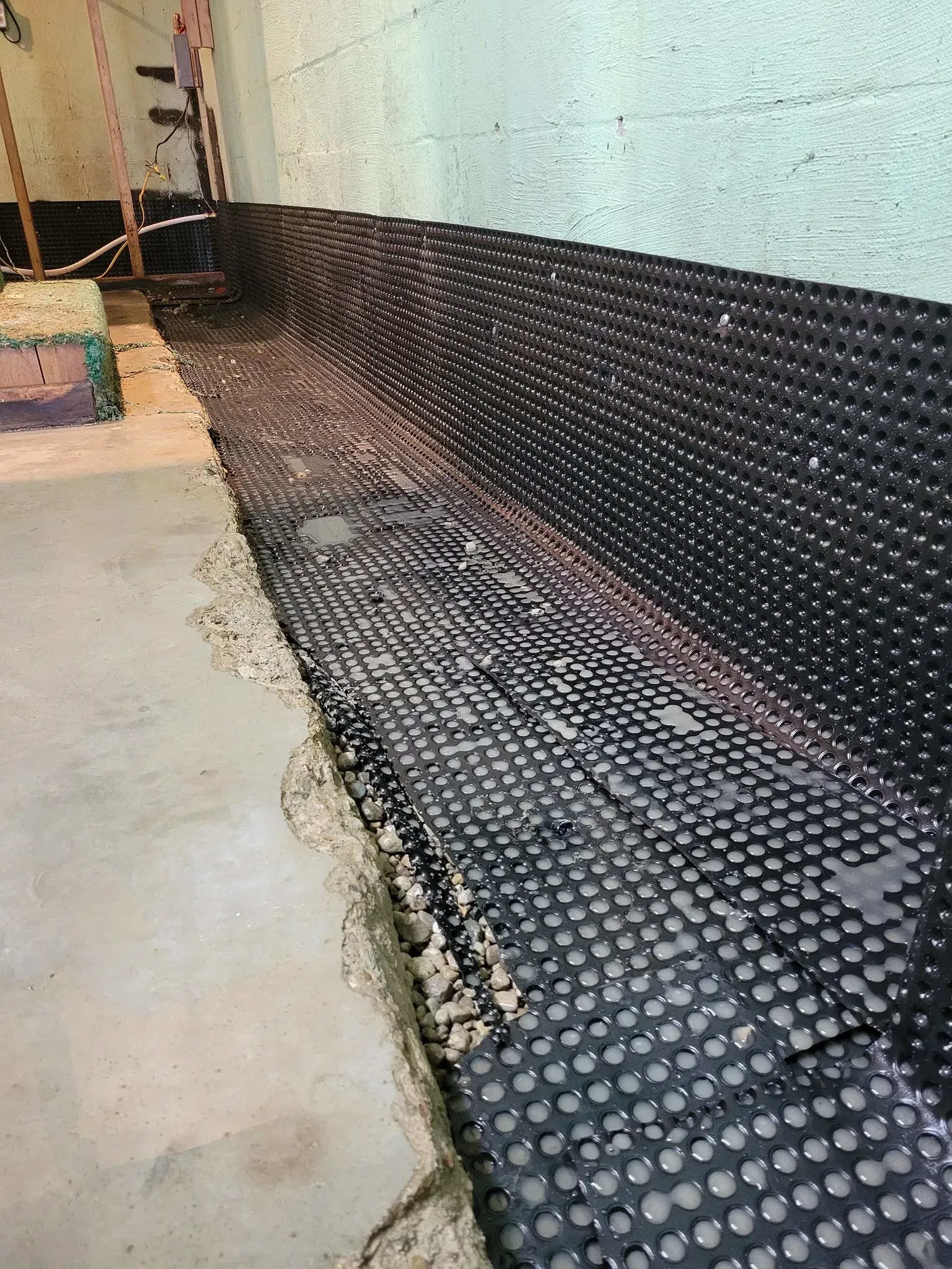 Black drainage mat along a wall beside a concrete walkway and garden bed