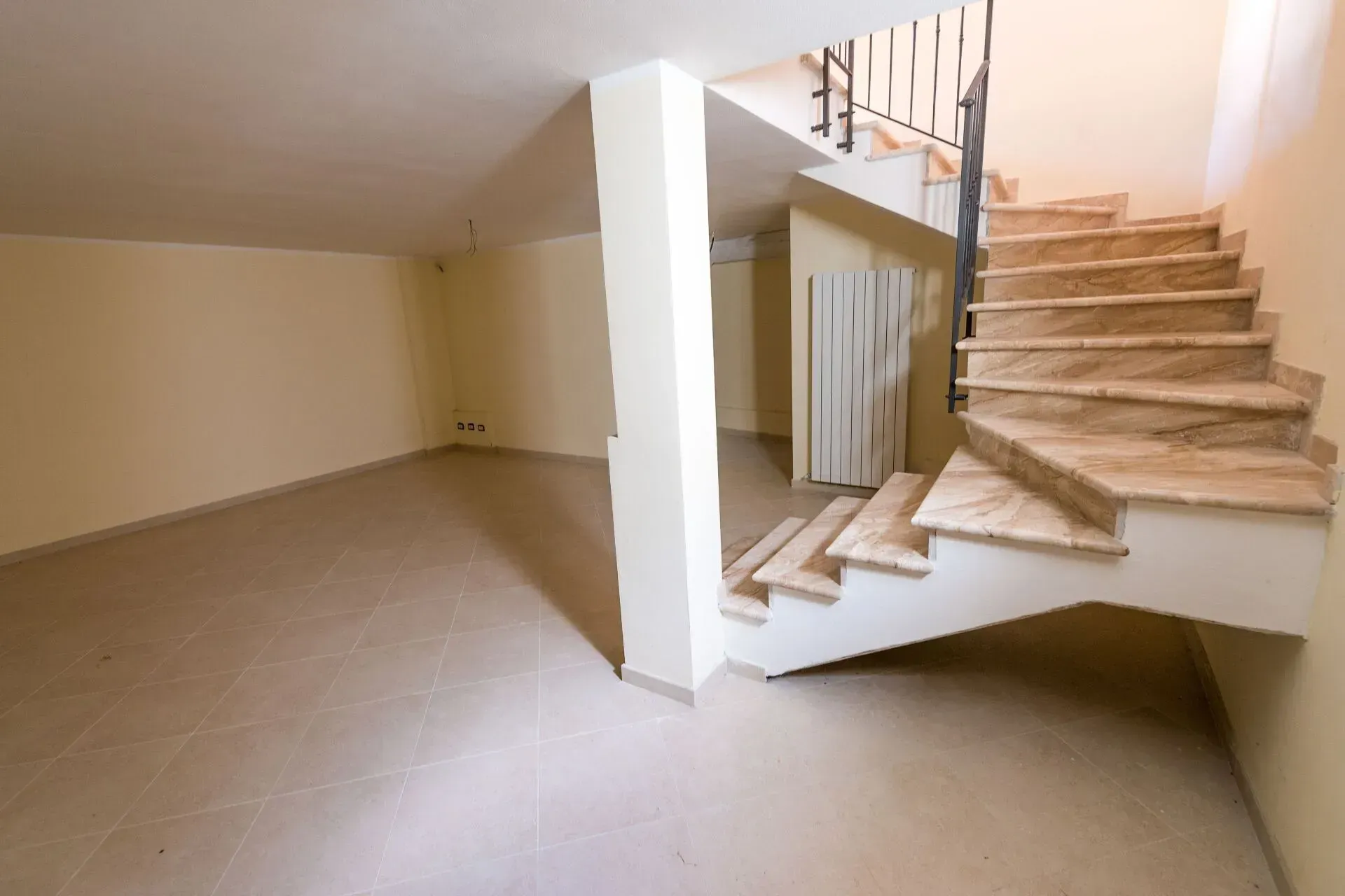 Empty beige room with tiled floor and a curved staircase with a white railing