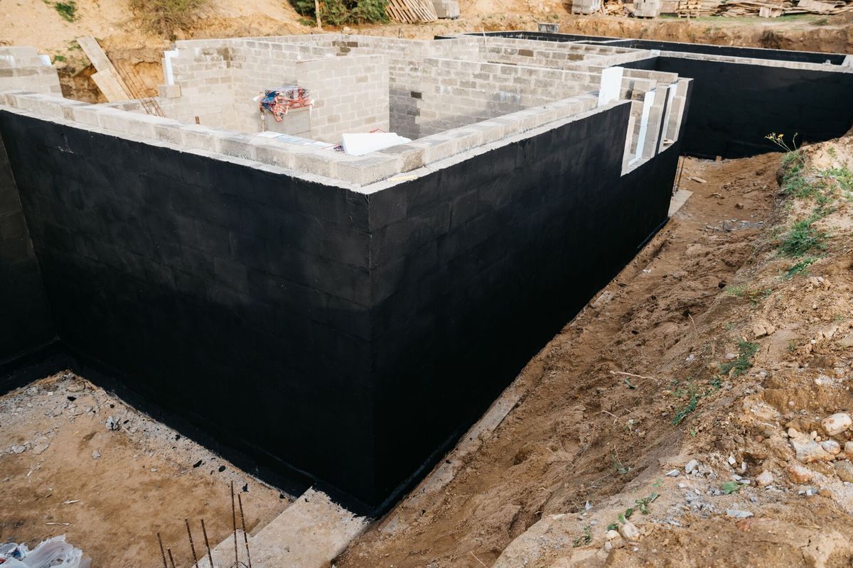 Concrete foundation walls coated with black waterproofing at a construction site