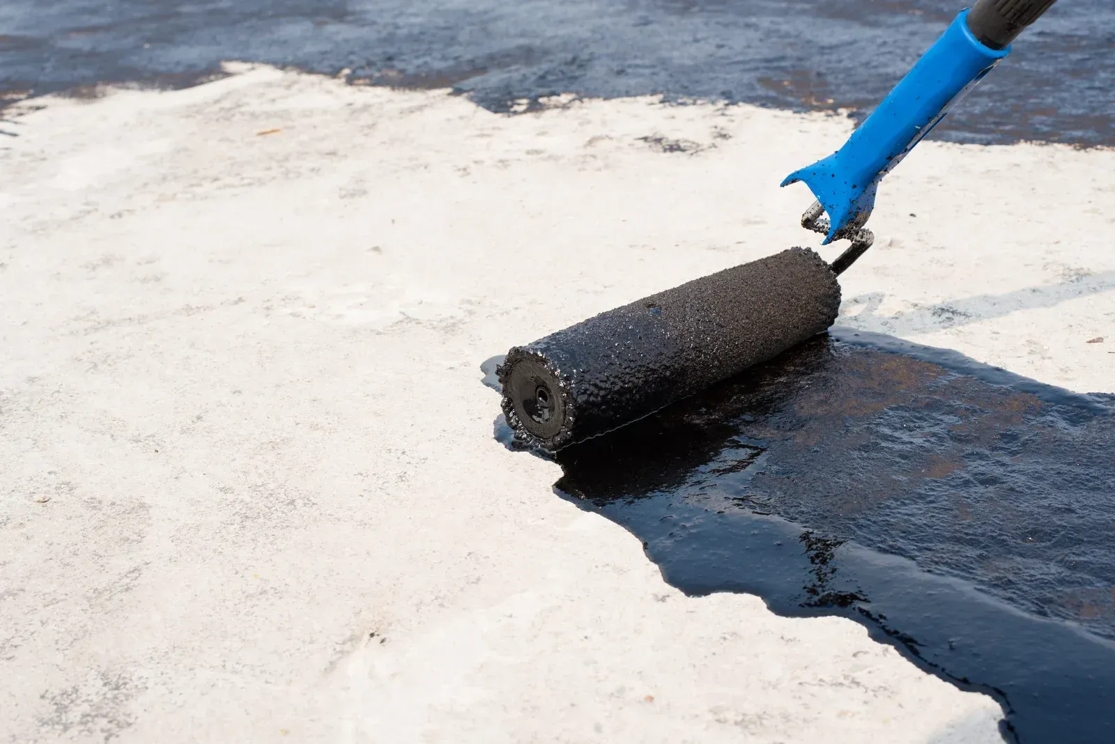 Person using a roller to apply black coating on a white surface outdoors