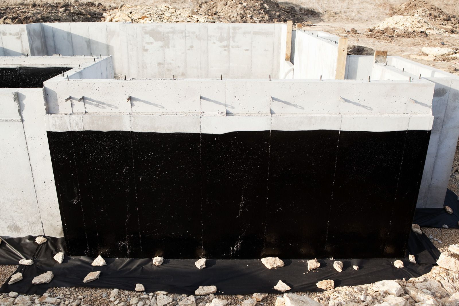 Black waterproofing on concrete foundation walls at a construction site