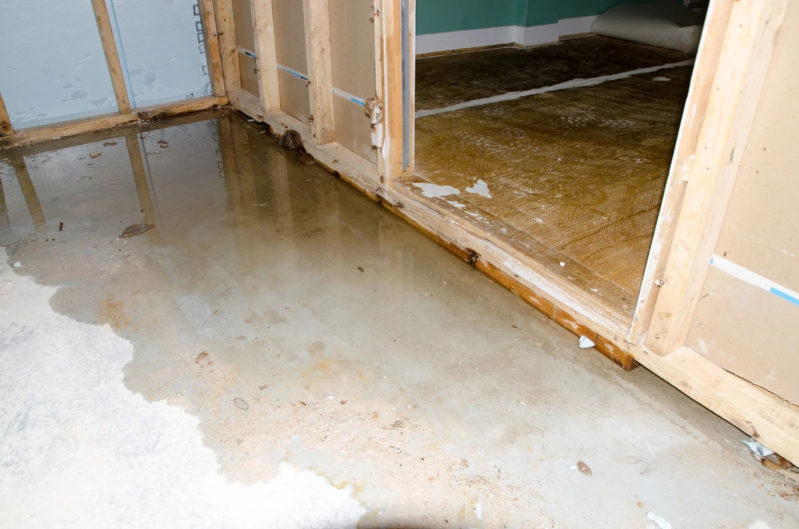 Water-damaged room with wet concrete floor and exposed wall framing around a doorway