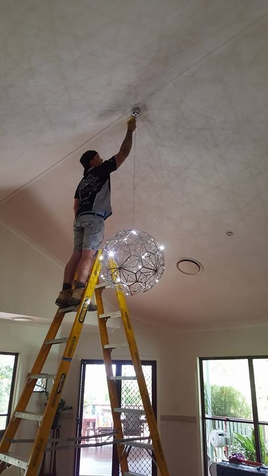 Man Standing On A Ladder Fixing A Light Fixture — Stand Fast Electrical Pty Ltd in Stanthorpe, QLD