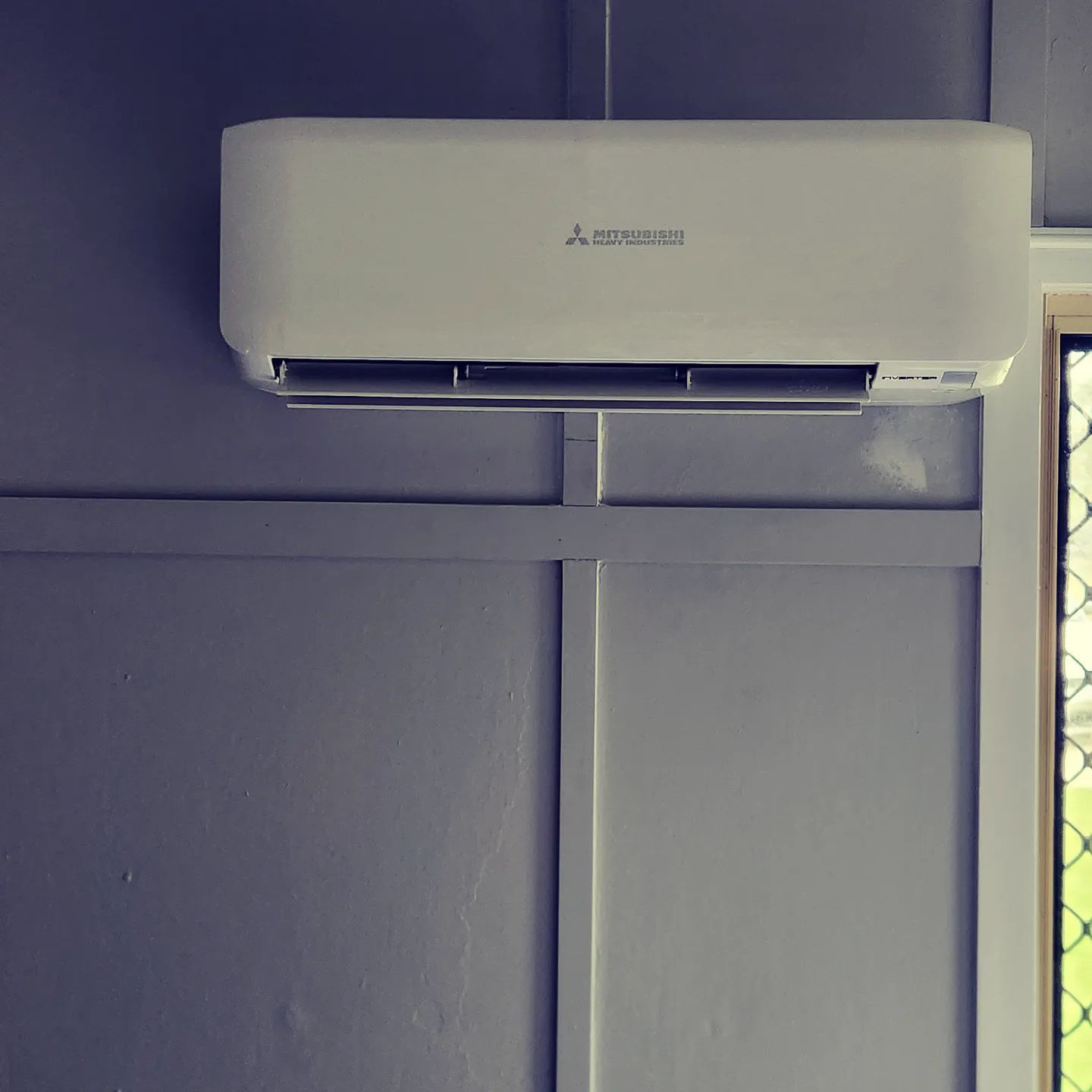 White Air Conditioner Is Mounted On A Wall Next To A Window — Stand Fast Electrical Pty Ltd in Killarney, QLD