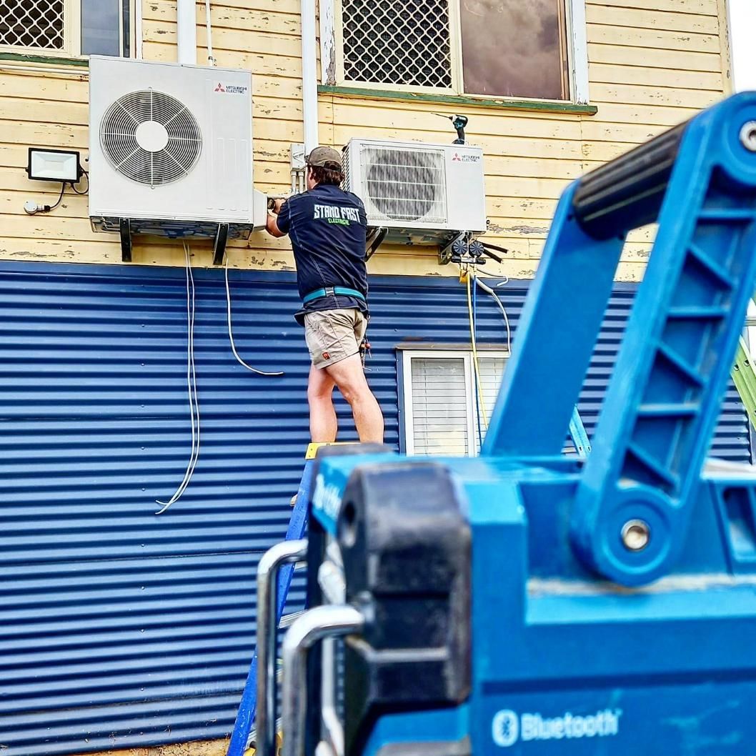 Man On A Ladder Fixing Air Conditioner — Stand Fast Electrical Pty Ltd in Warwick, QLD