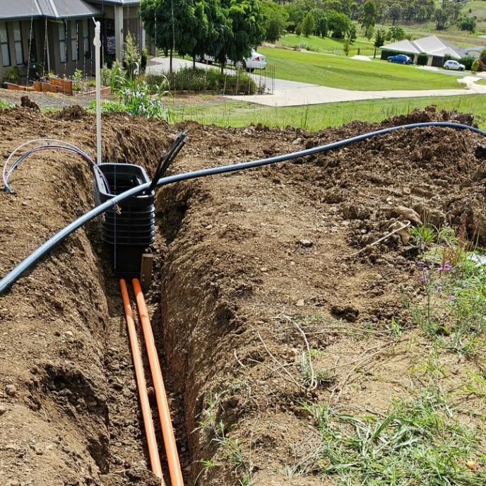 A Bunch Of Pipes Are Laying In The Dirt in A Trench — Stand Fast Electrical Pty Ltd in Inglewood, QLD