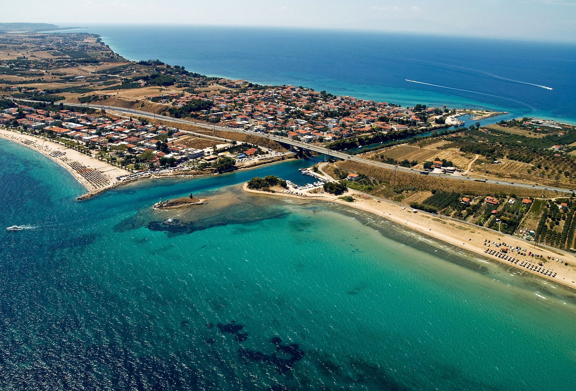 Aerial view of a turquoise coastal inlet with sandy beaches, a bridge, and nearby buildings