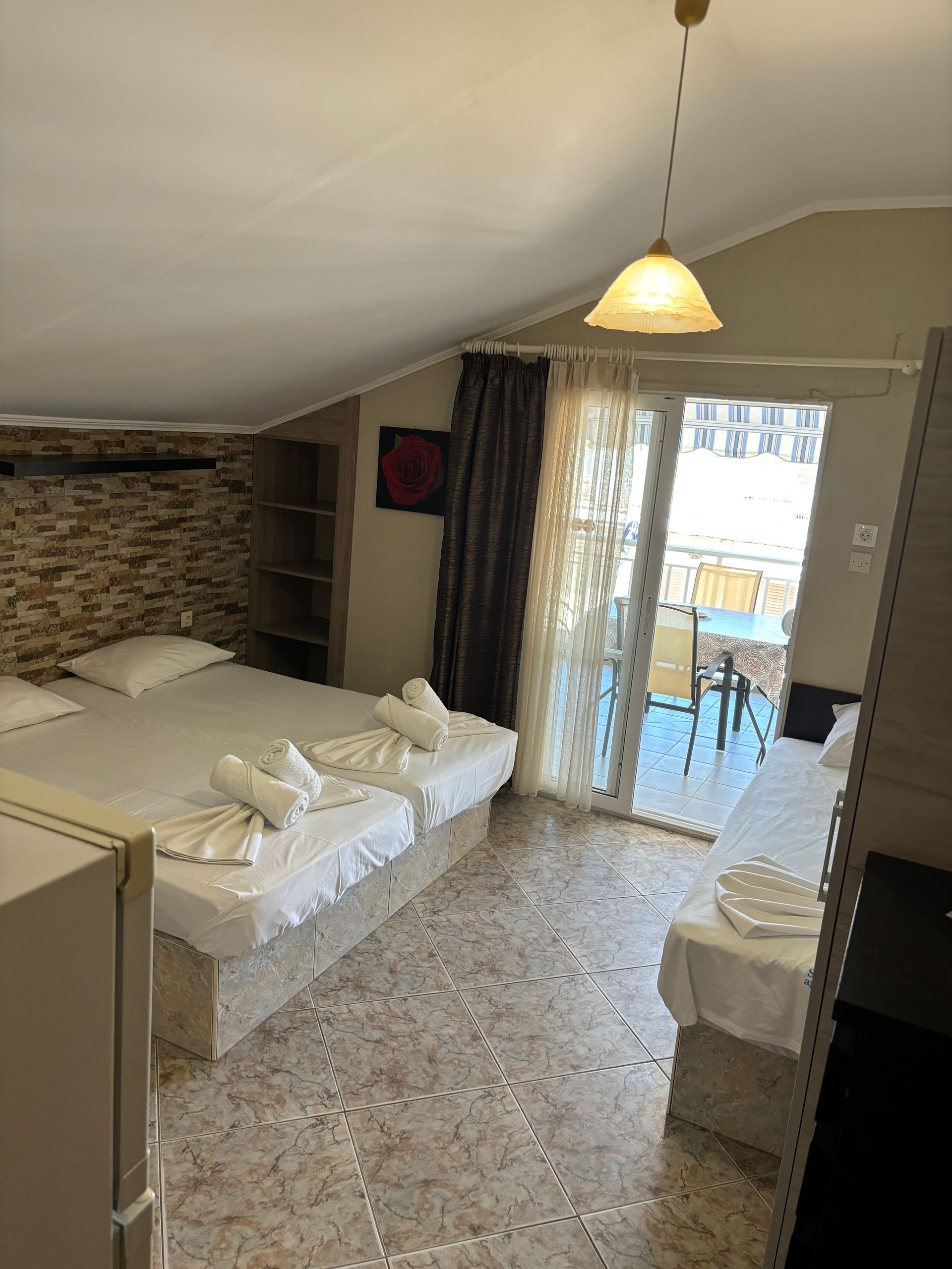 Small bedroom with an unmade bed, brick accent wall, hanging light, and balcony doors open to sunlight