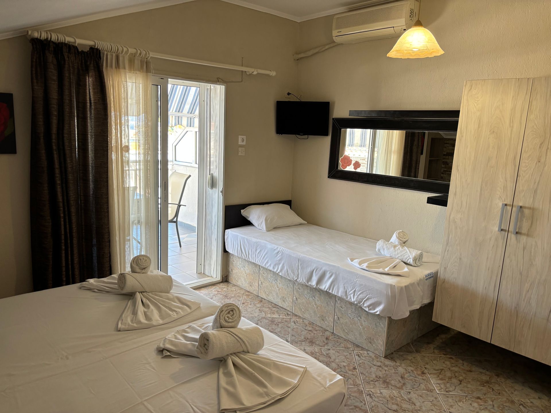 Small hotel room with two single beds, a large mirror, and a sliding door to a balcony.