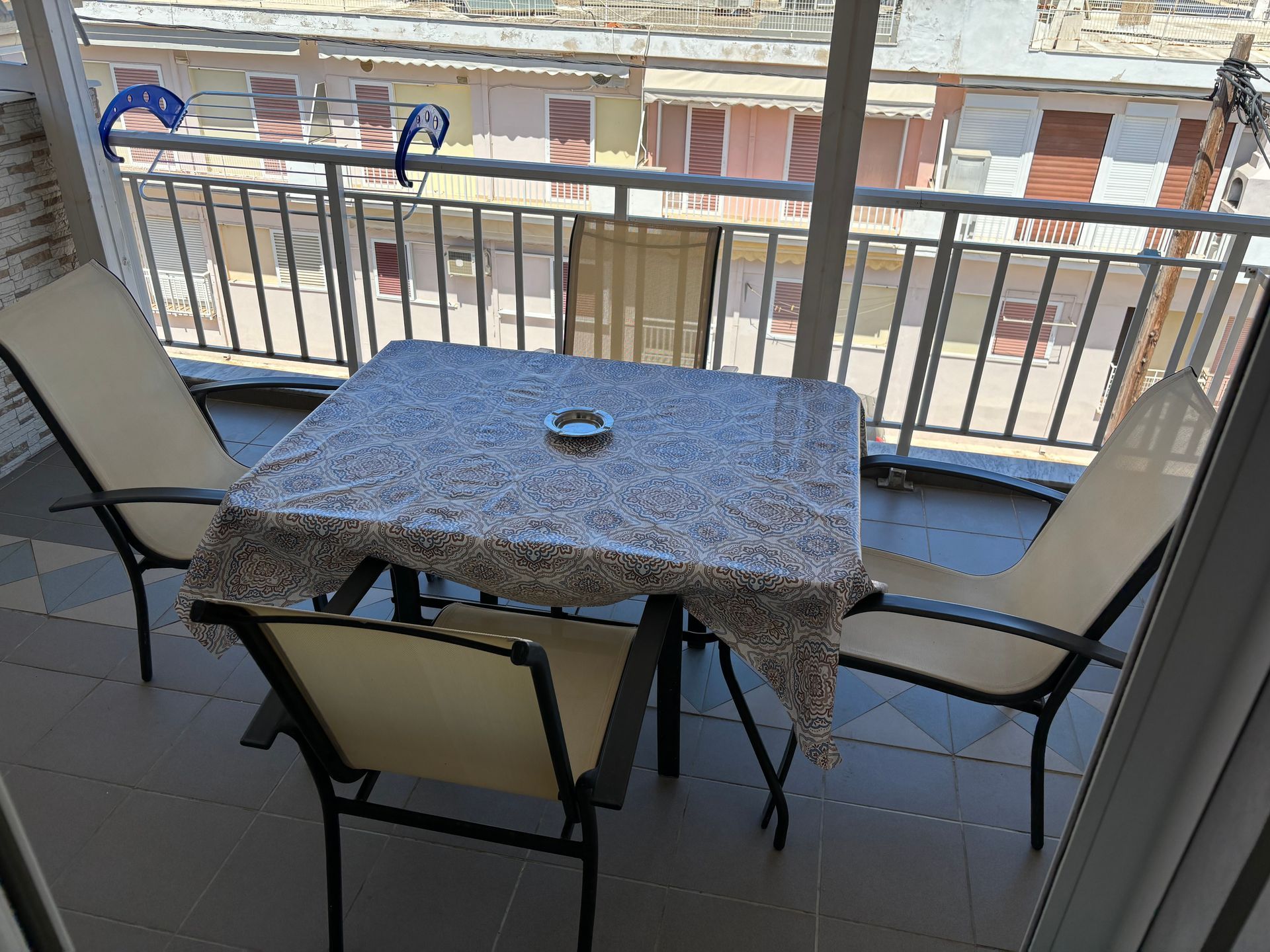 Balcony patio table with four chairs and a small ashtray, overlooking a street below
