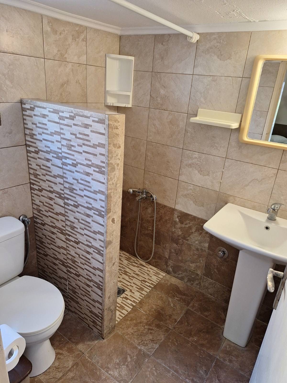 Small tiled bathroom with toilet, shower area, and pedestal sink next to a mirror.