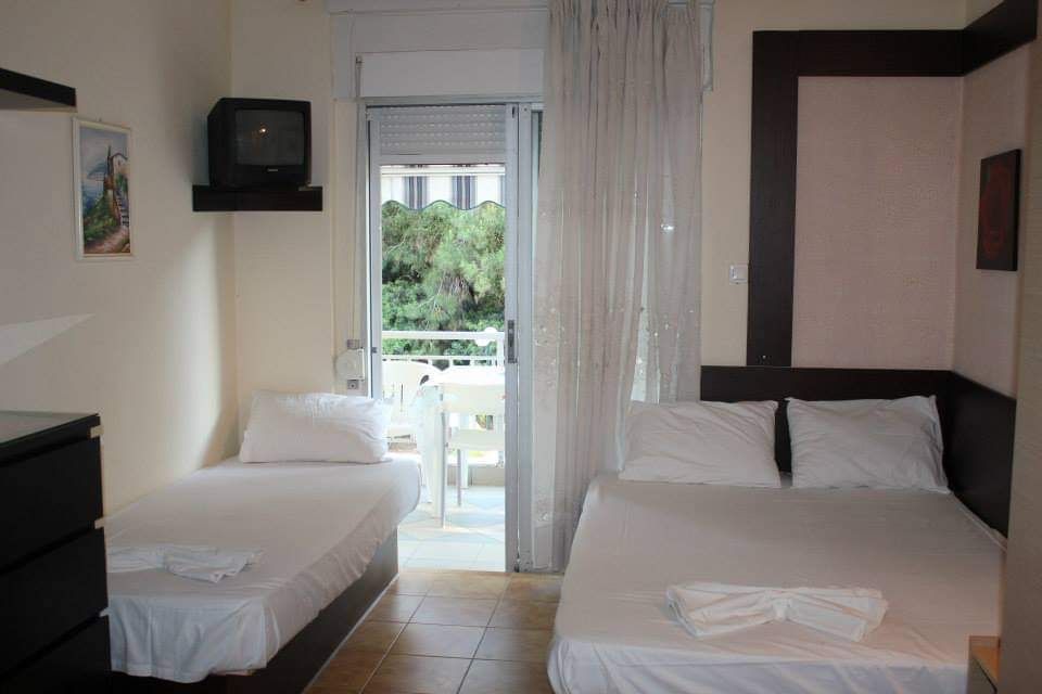 Small hotel room with two single beds, white linens, and a balcony door to greenery.