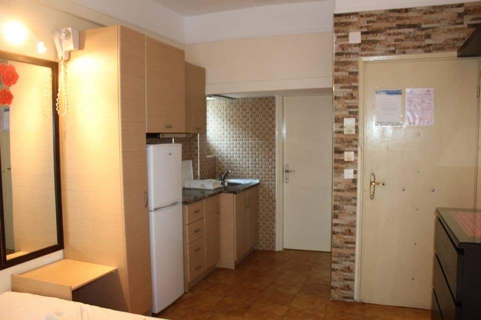 Small kitchen with beige cabinets, white fridge, tiled backsplash, and a stone accent wall near a door.