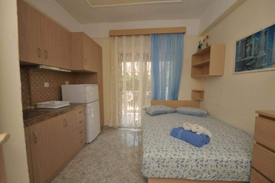Small bedroom with twin bed, kitchenette, tiled floor, and balcony door with curtains