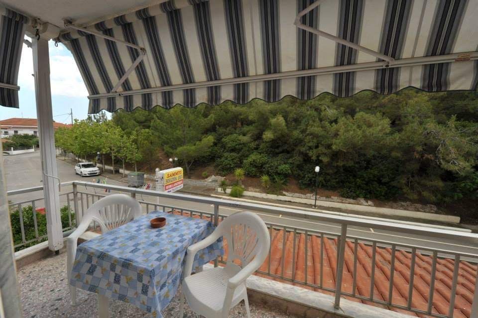 Covered balcony with striped awning, table and chairs, and a view of trees and rooftops.