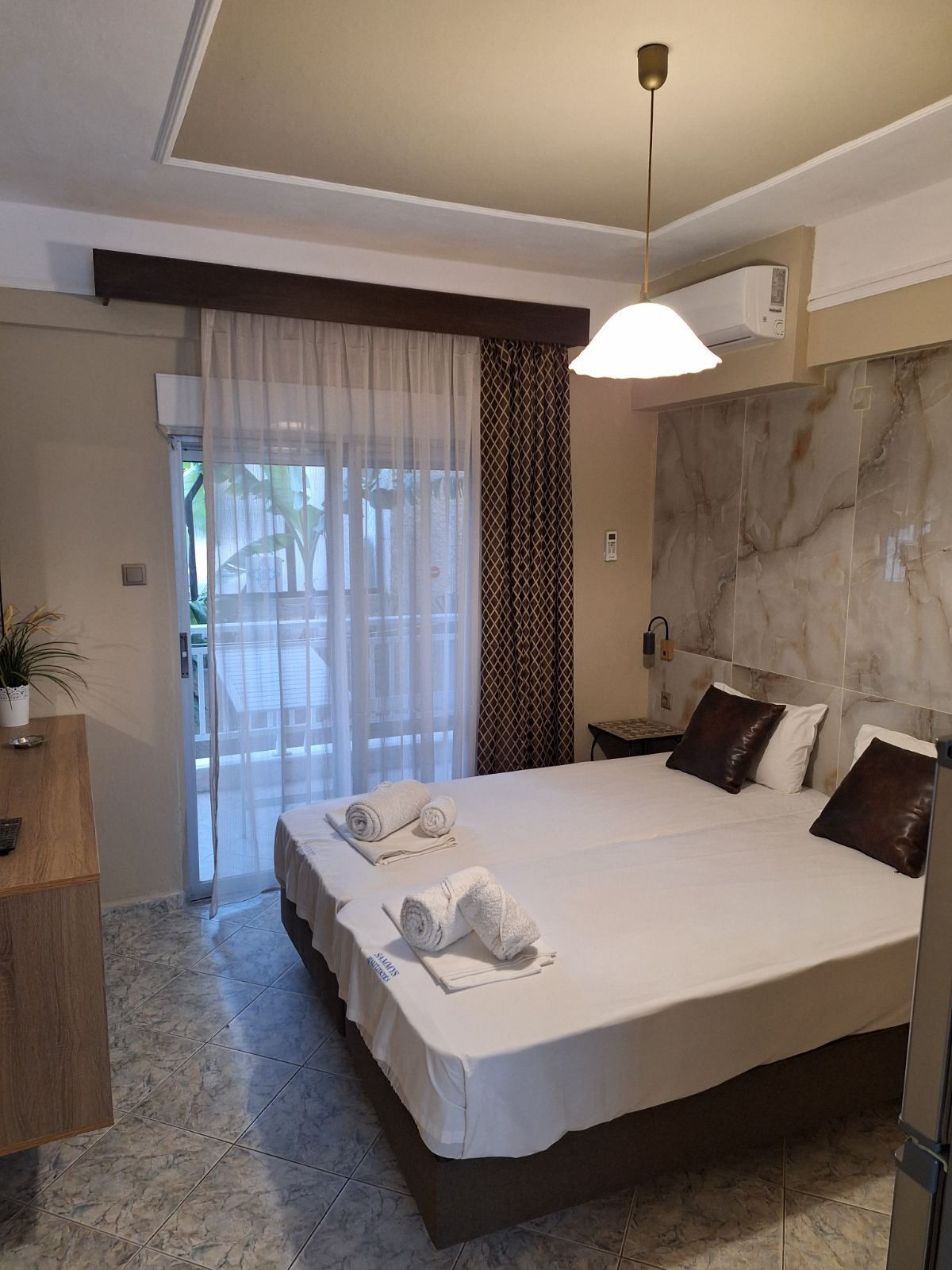 Bright bedroom with a bed, wall mural, balcony door, and hanging light.