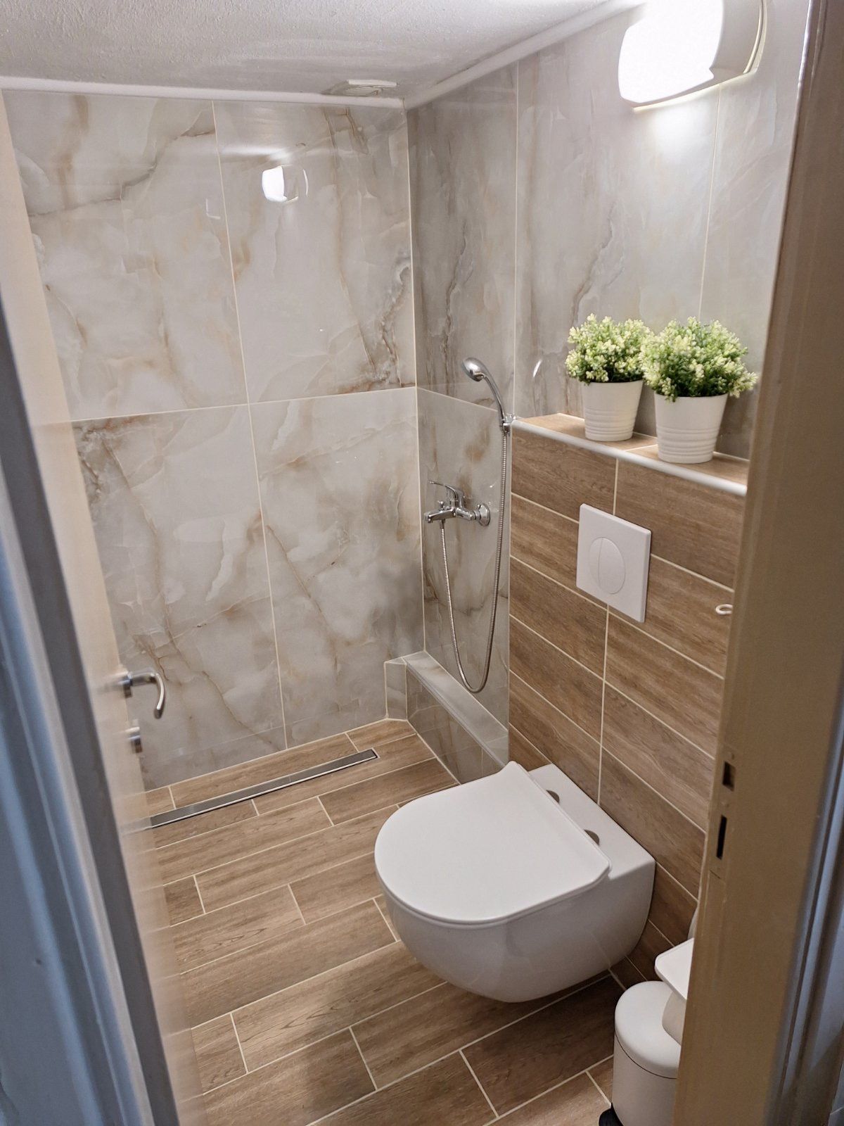 Modern bathroom with walk-in shower, wall-mounted toilet, and wood-look tile accents