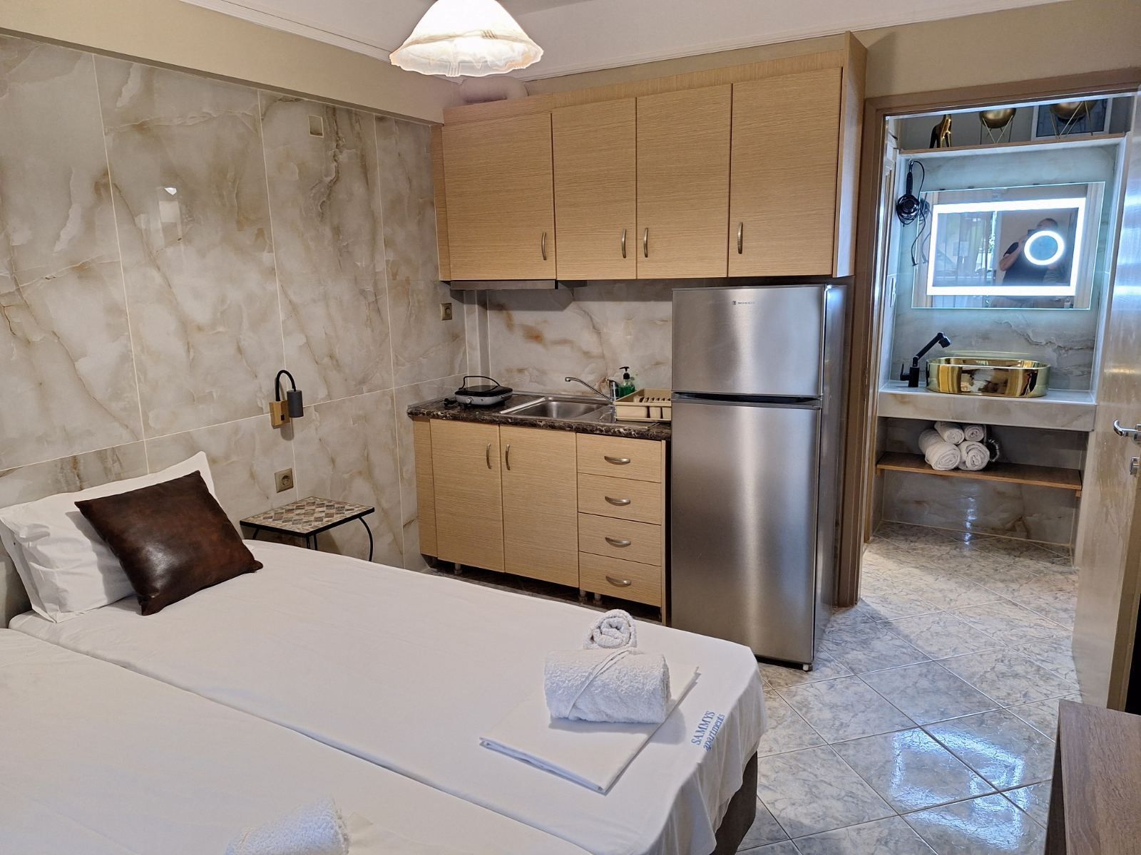 Small studio room with a bed, kitchenette, refrigerator, and bathroom doorway.