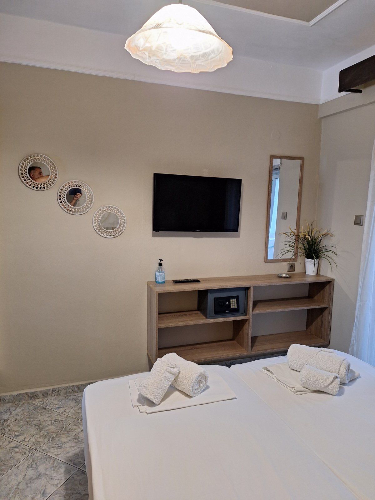 Bedroom with wall-mounted TV, dresser, mirror, and bed with folded towels near a window.