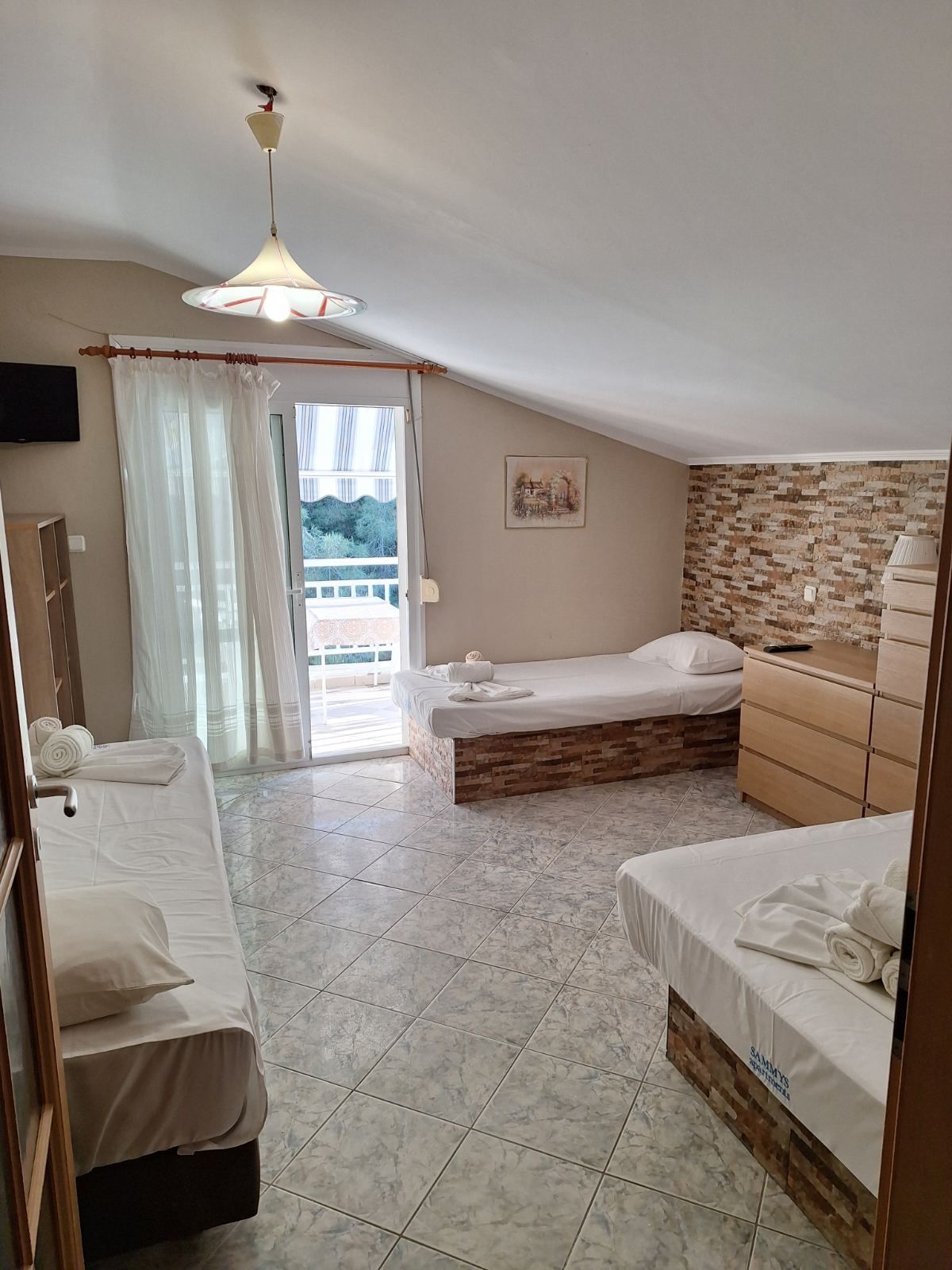 Small bedroom with three beds, tiled floor, stone accent wall, and a sliding door to a balcony.