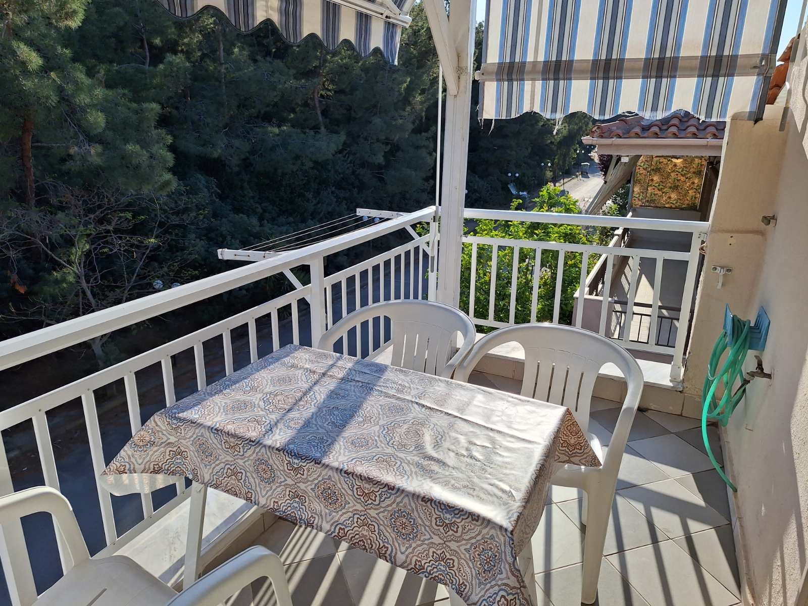 Balcony patio with table, white chairs, striped awning, and city street view beyond the railing