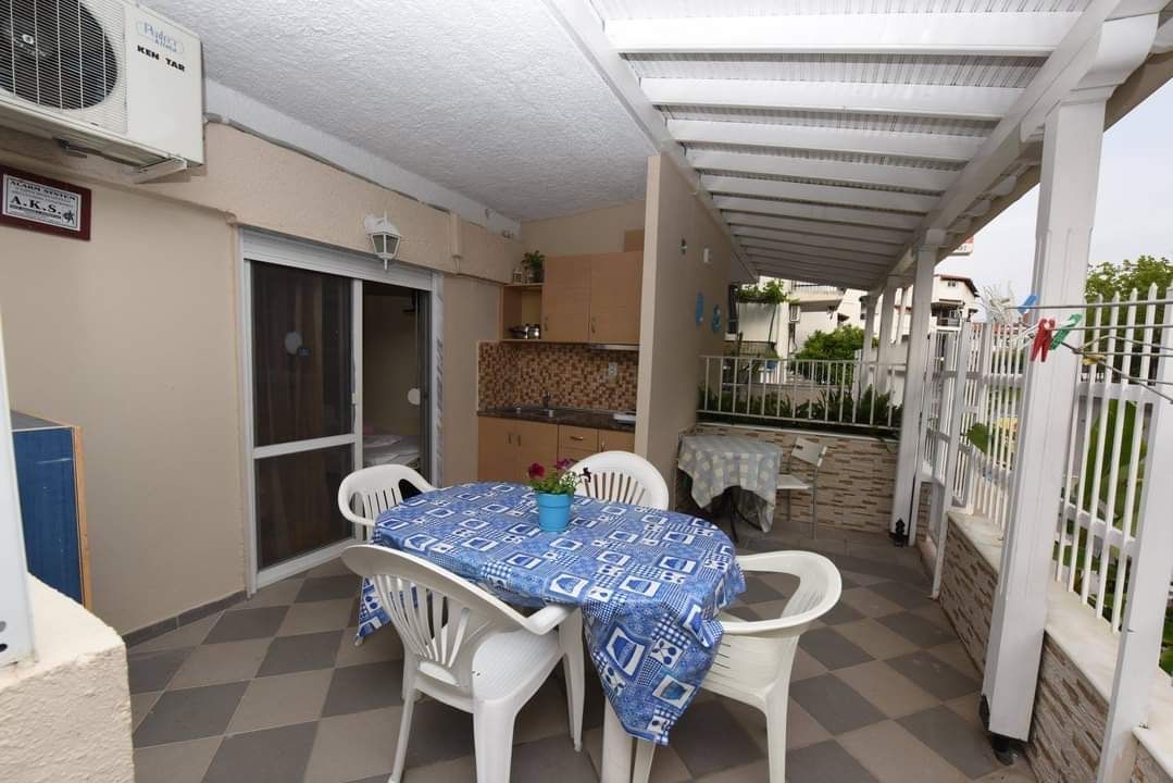 Covered patio with white plastic table and chairs, blue tablecloth, and sliding glass doors beside a fenced walkway