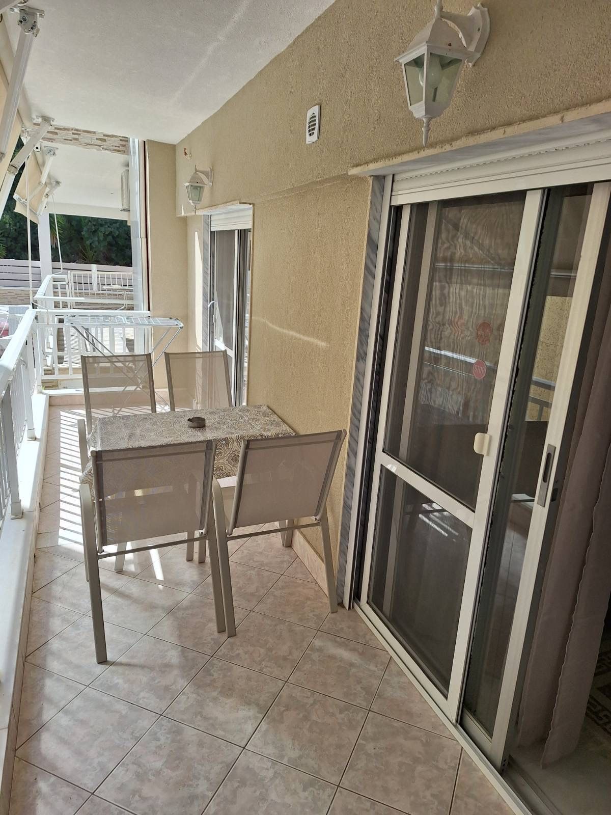 Covered balcony with table and chairs beside sliding glass doors and potted plants overlooking greenery