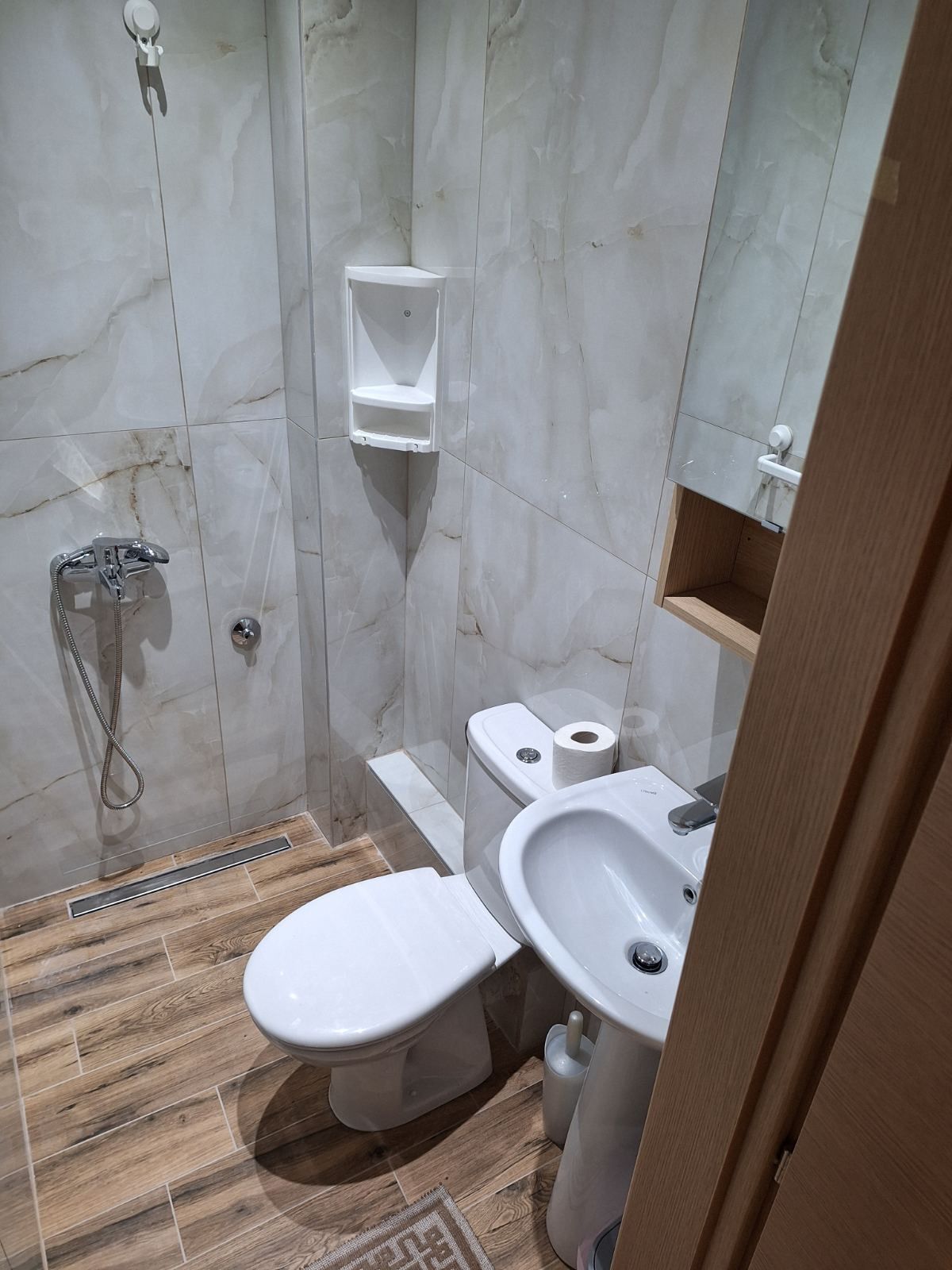 Small modern bathroom with toilet, sink, shower fixture, and marble-look tiled walls