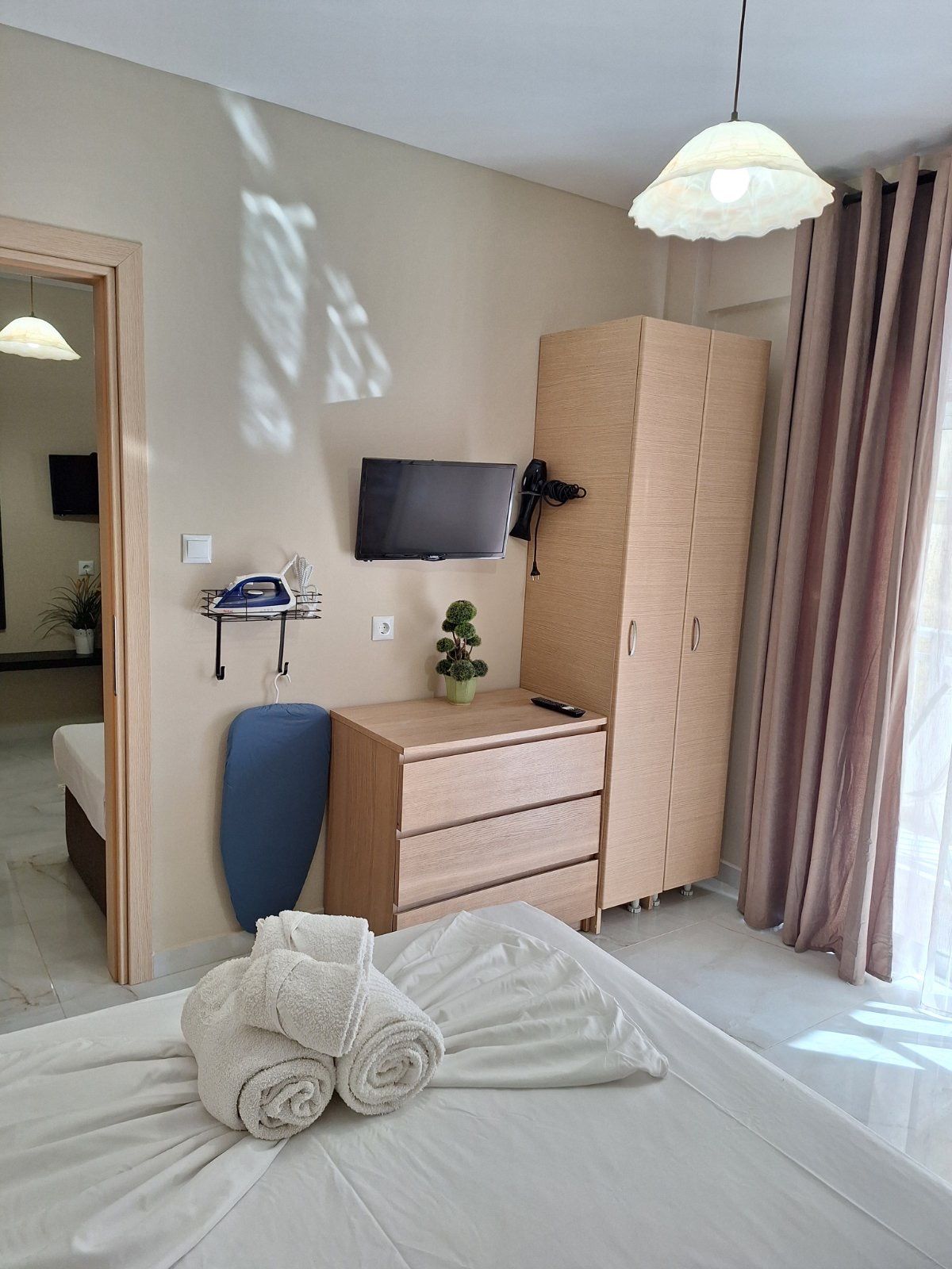 Cozy bedroom with bed, dresser, wall-mounted TV, wardrobe, and balcony curtains in soft beige tones