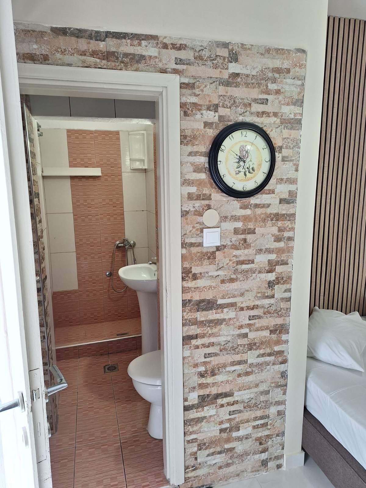 Bedroom doorway opening to a small bathroom with brick-pattern wall tile and a wall clock nearby