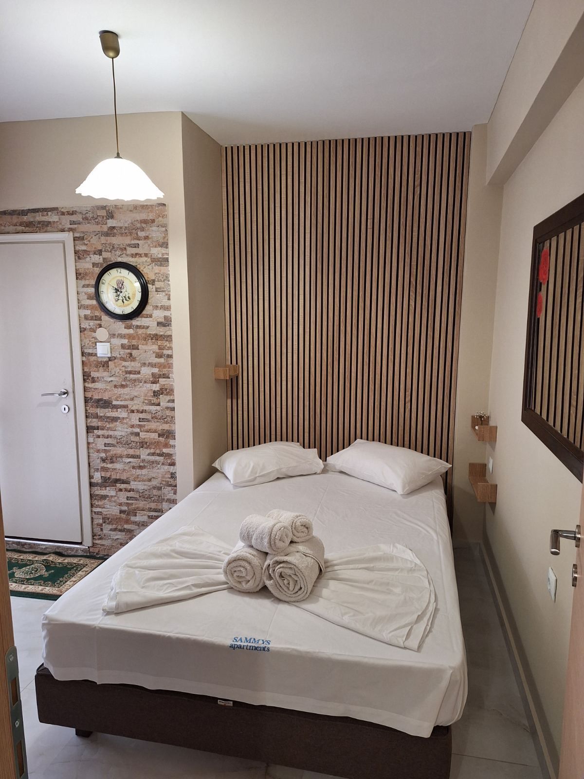 Cozy bedroom with a double bed, striped accent wall, brick doorway, and hanging pendant light.