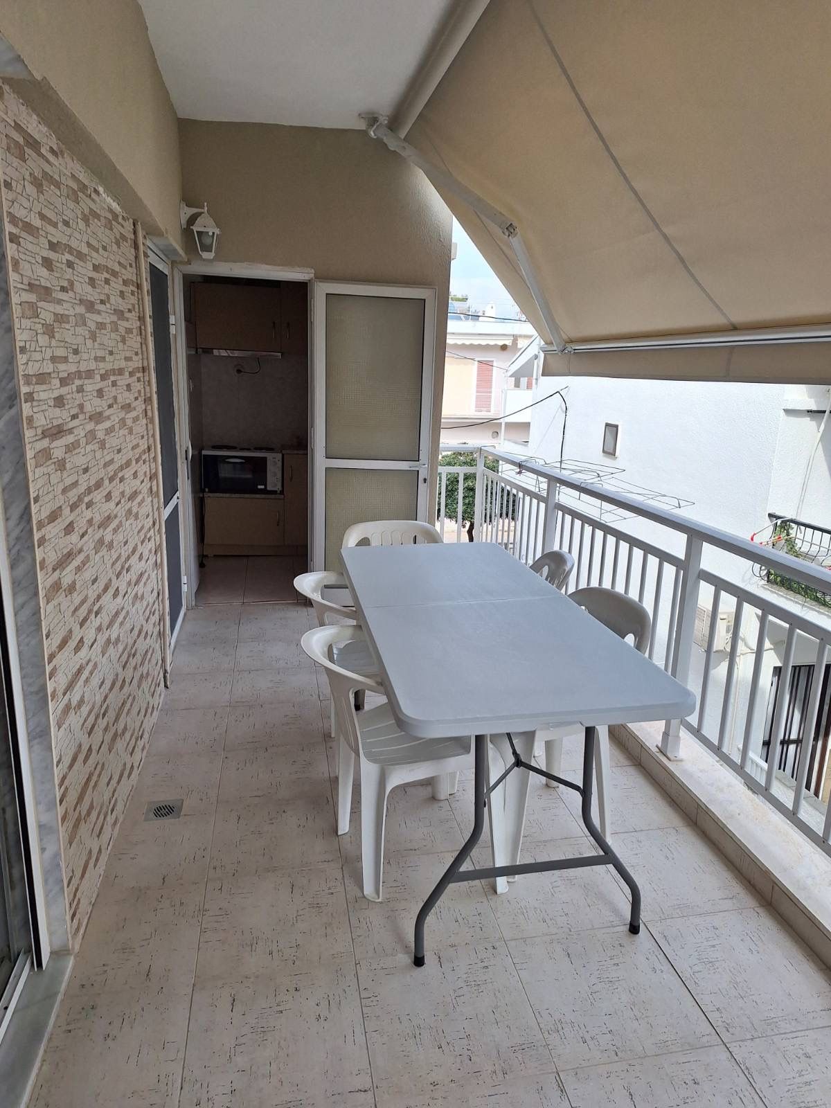 Balcony with a table and two stools beside a railing, overlooking neighboring buildings.