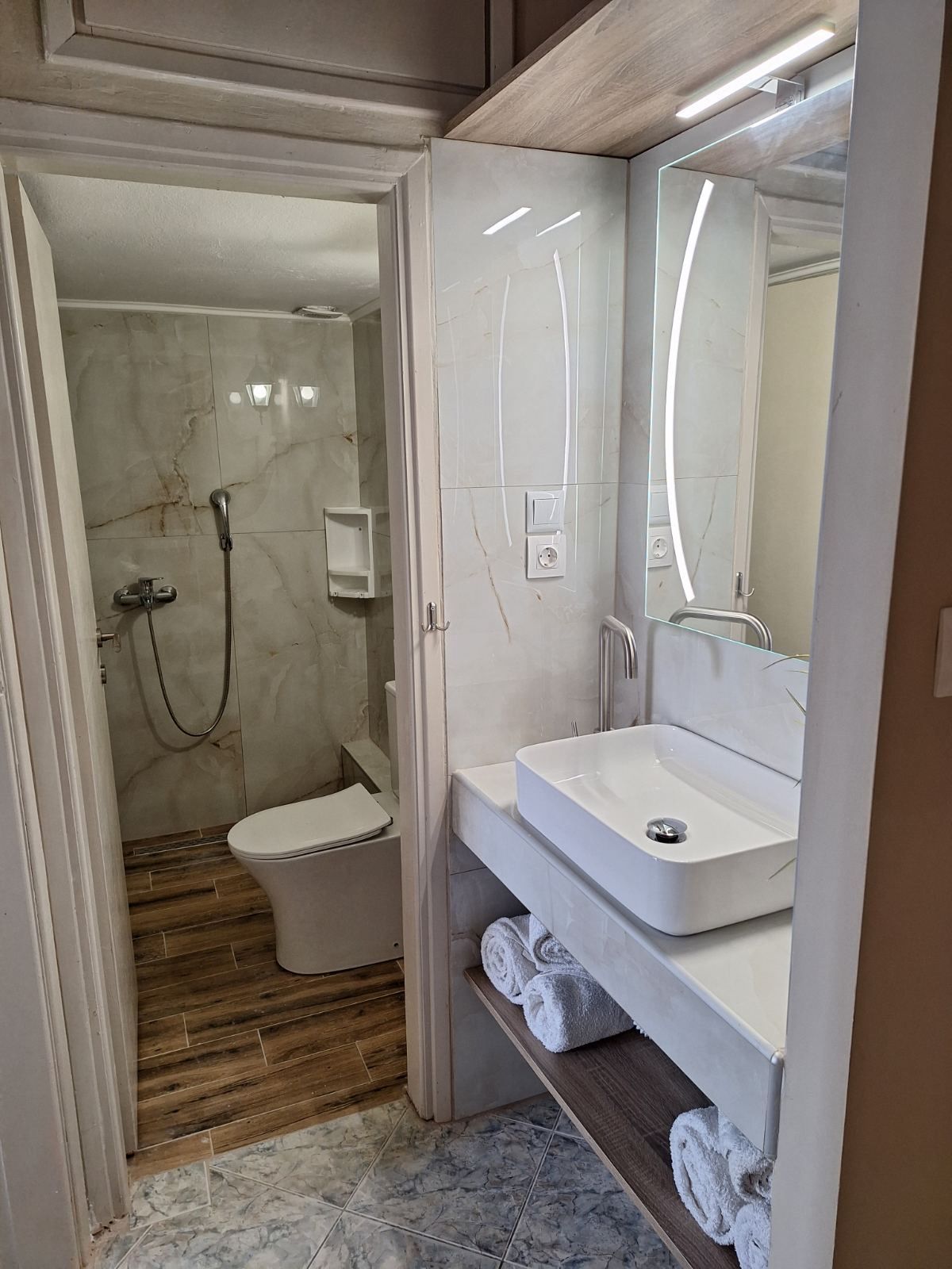Compact bathroom with shower, toilet, and white sink in a narrow tiled room