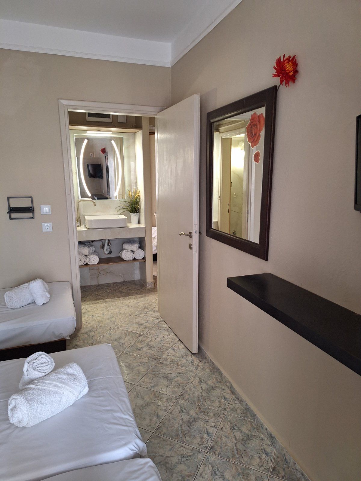 Hotel room with twin beds, mirror, open bathroom door, and beige walls