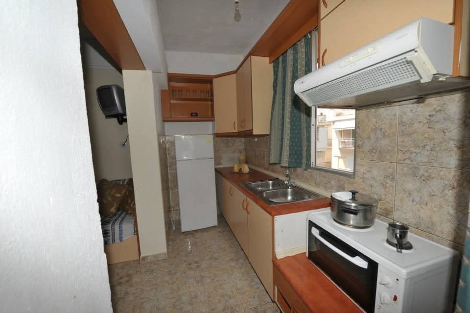 Narrow kitchen with white appliances, wood cabinets, tiled floor, and window with green curtains