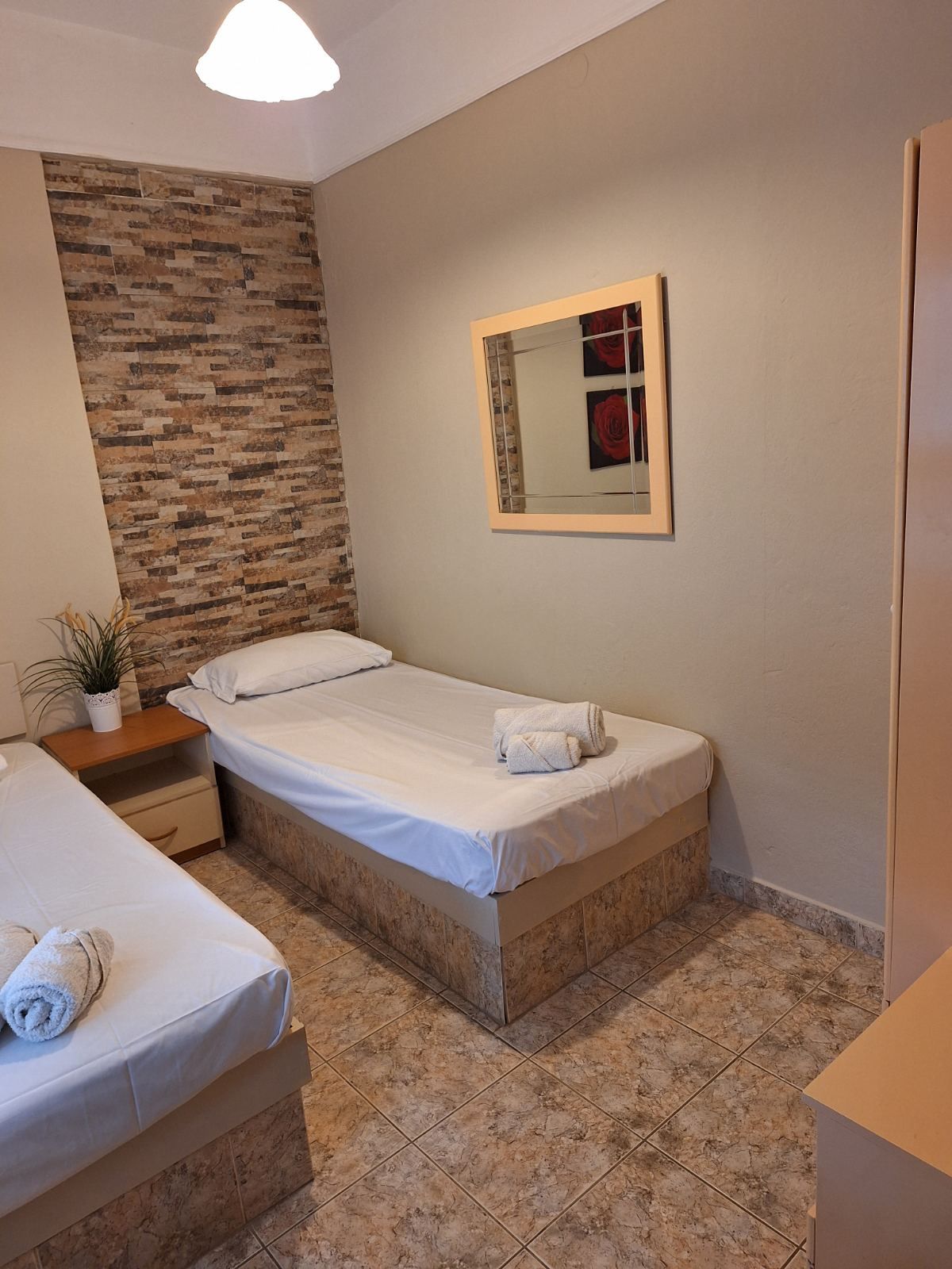 Small twin bedroom with two single beds, beige walls, patterned floor, and a wall mirror.