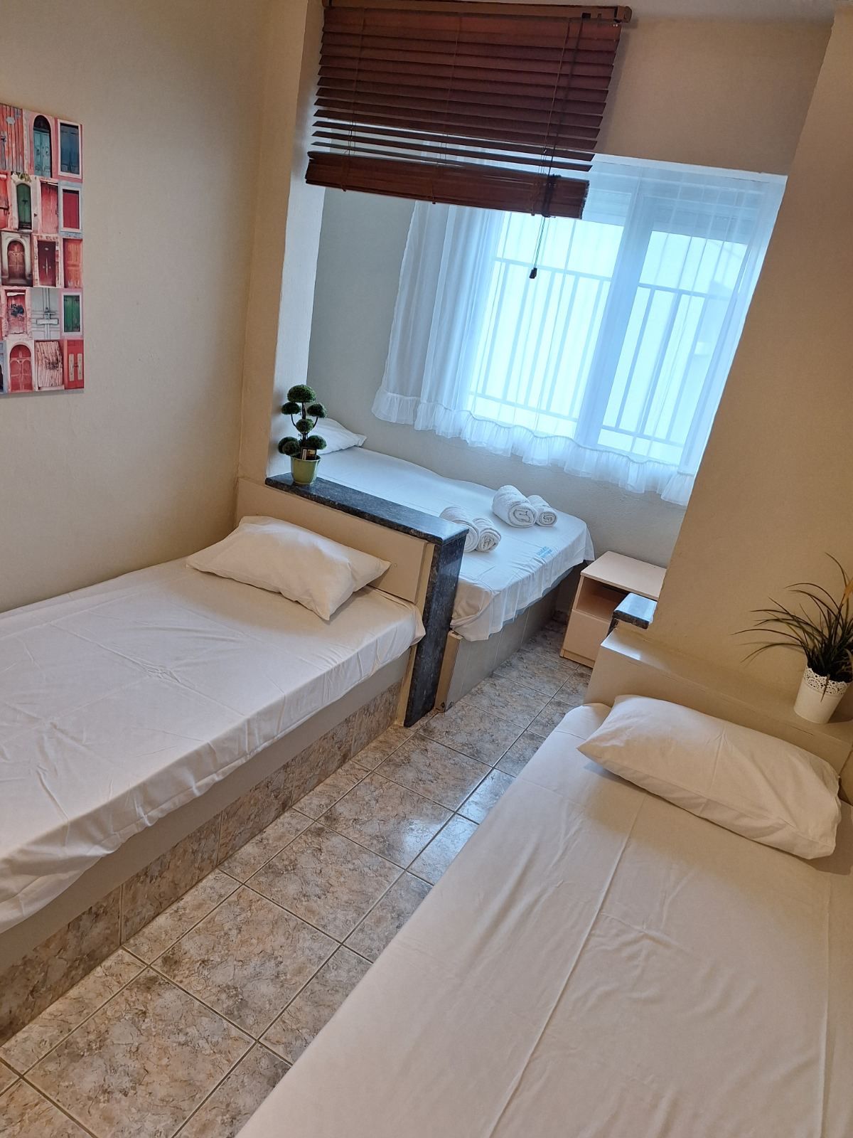 Small bedroom with two single beds, white bedding, window, and wooden blinds.