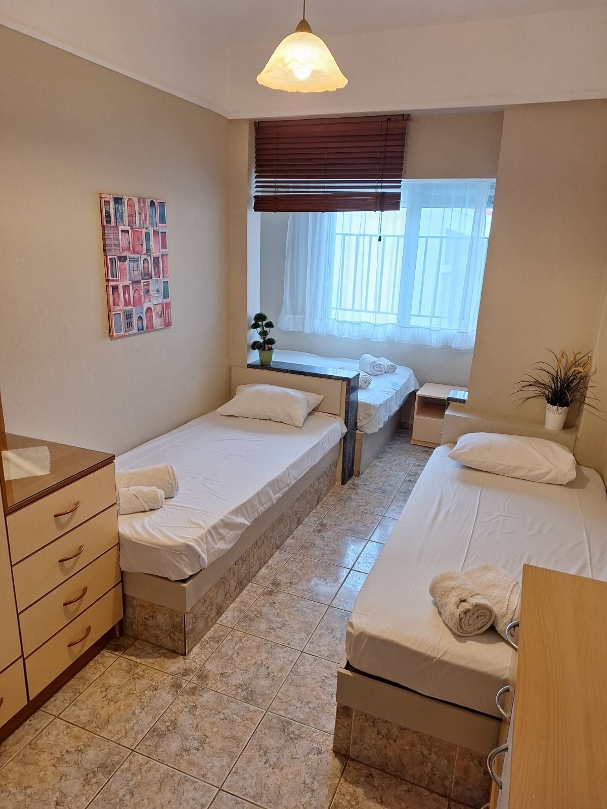 Shared bedroom with four single beds, dresser, and window with blinds and curtains.