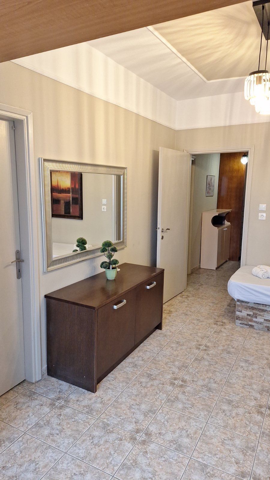 Bright hallway with beige walls, dark wood cabinet, mirror, doorway, and patterned tile floor