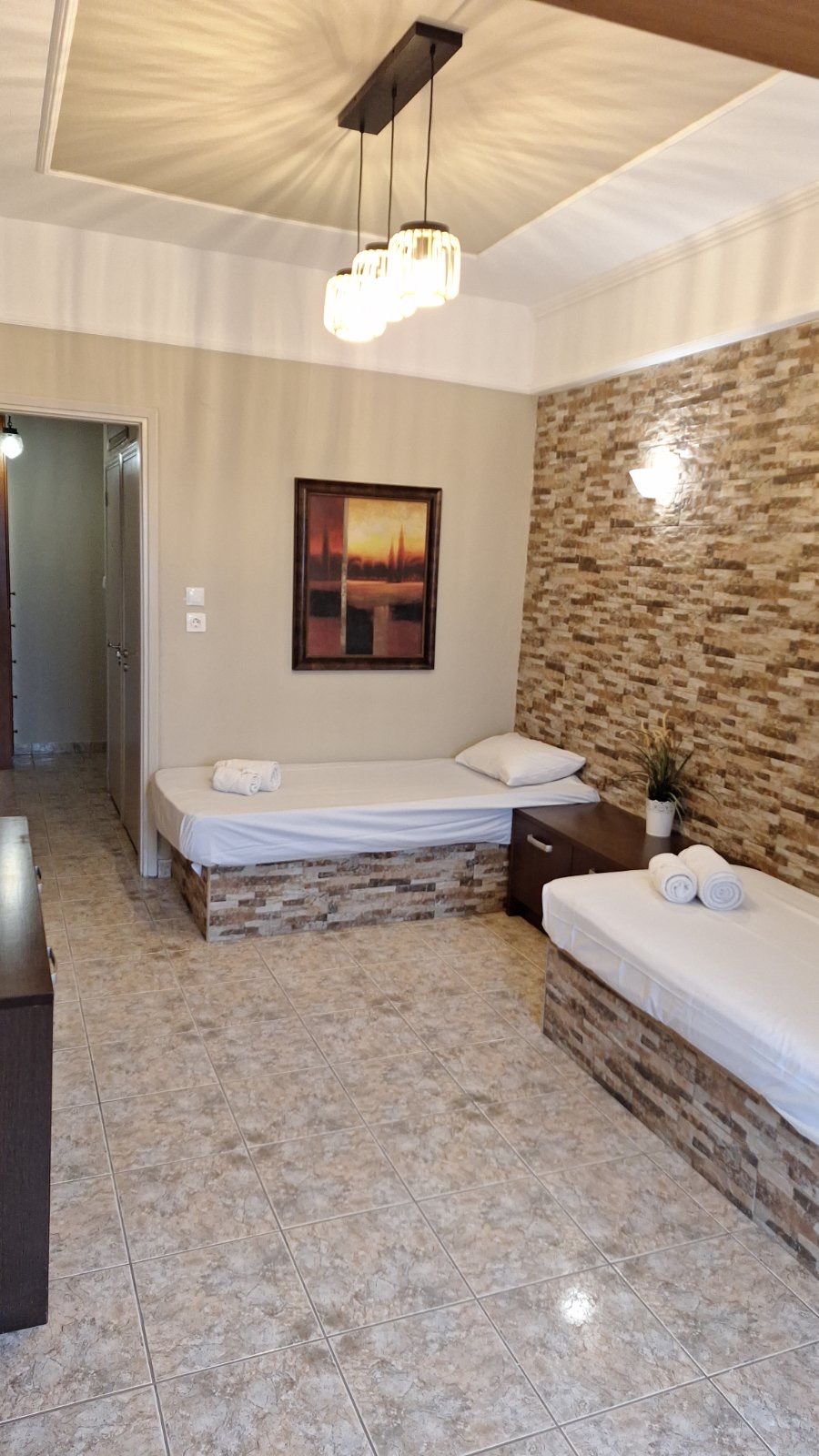 Modern bedroom with two single beds, stone accent wall, and hanging ceiling light