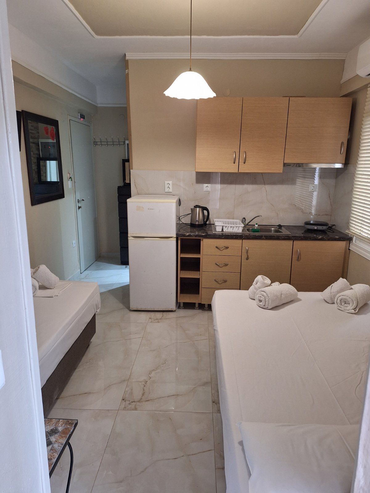 Small room with two single beds, kitchenette, blue curtains, and a hanging light.