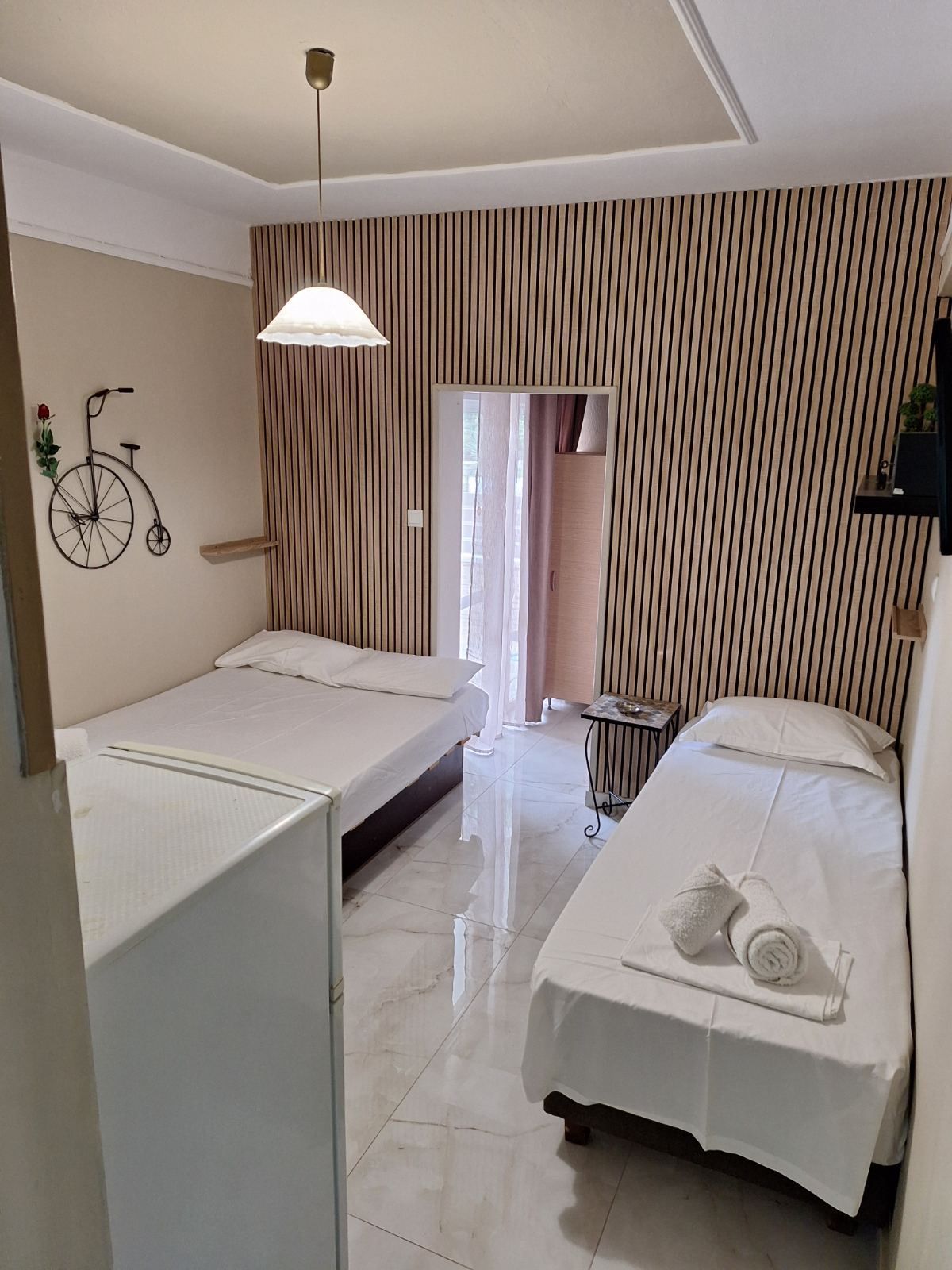 Small blue bedroom with two single beds, tiled floor, and a window with sheer curtains.