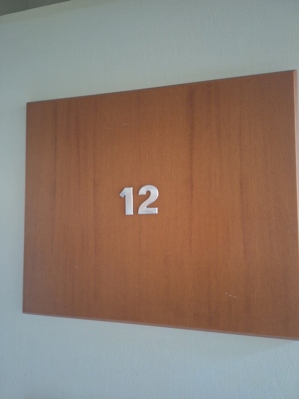 Brown wooden wall plaque with the number 12 on a light-colored wall